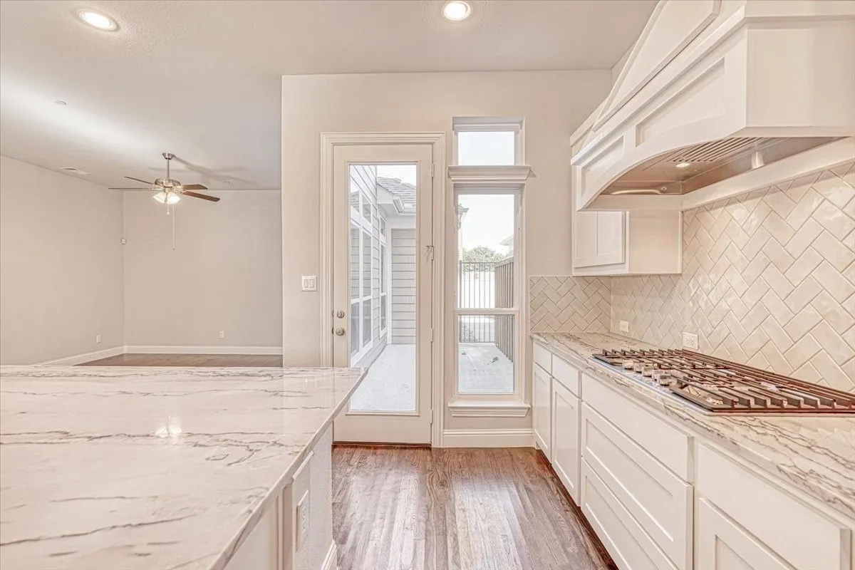 Kitchen featuring custom range hood, wood-type flooring, stainless steel gas cooktop, tasteful backsplash, and ceiling fan