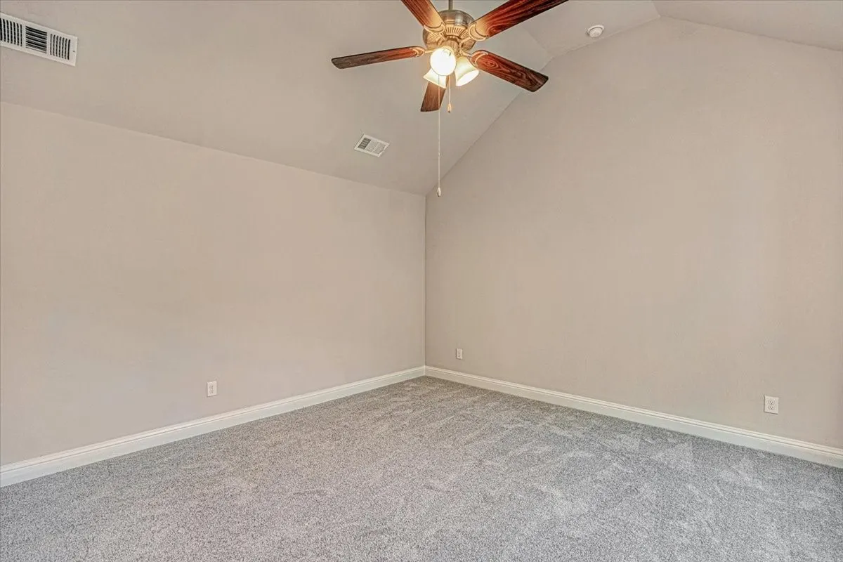 Carpeted empty room with high vaulted ceiling and ceiling fan