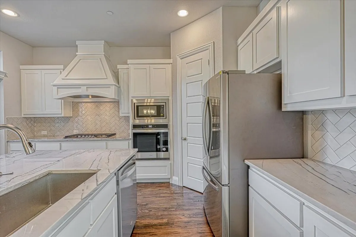 Kitchen with premium range hood, dark hardwood / wood-style flooring, backsplash, sink, and appliances with stainless steel finishes