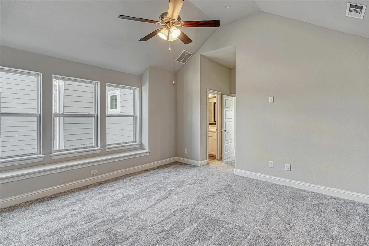 Carpeted empty room with ceiling fan and lofted ceiling