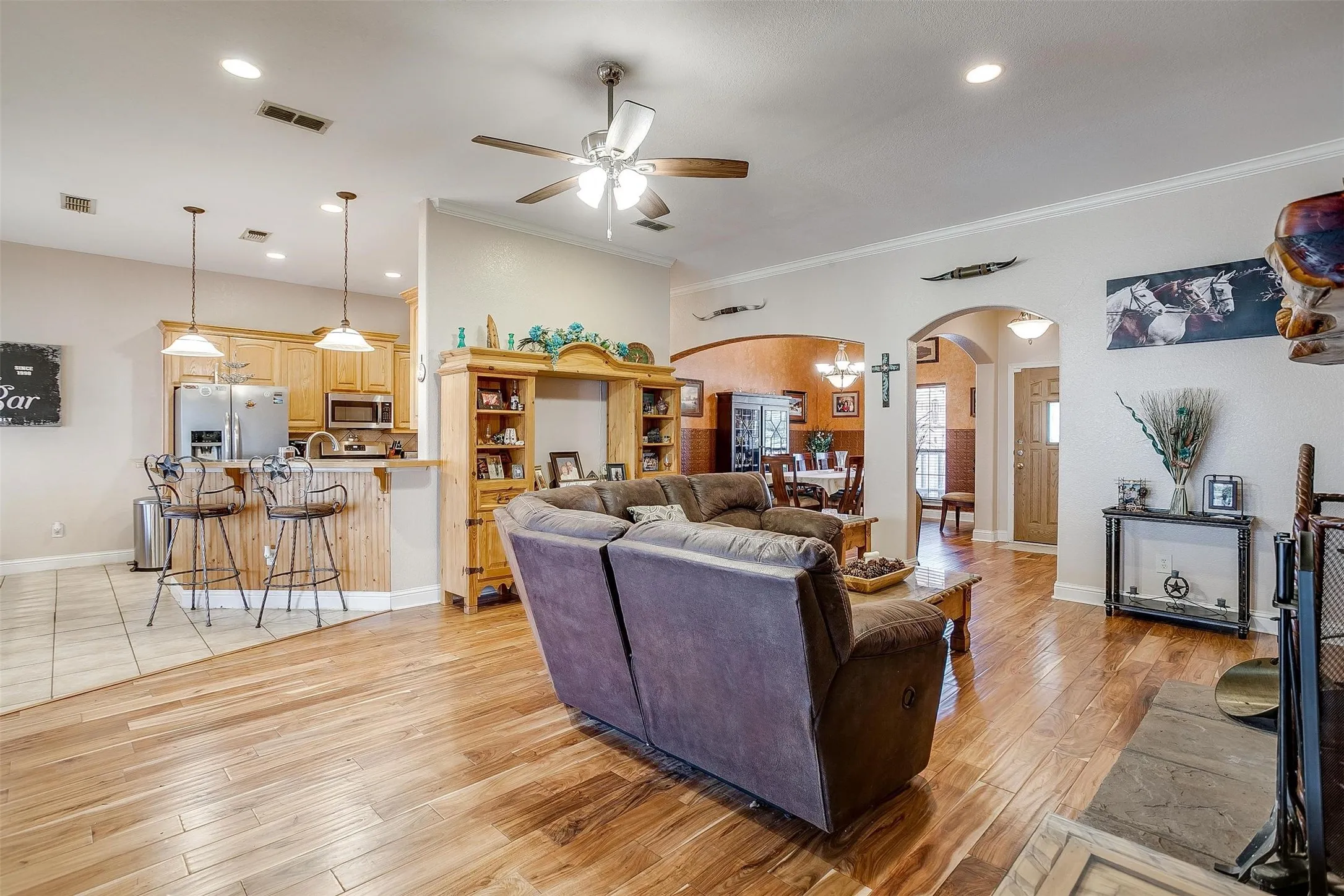 Living room with a ceiling fan, visible vents, arched walkways, and crown molding