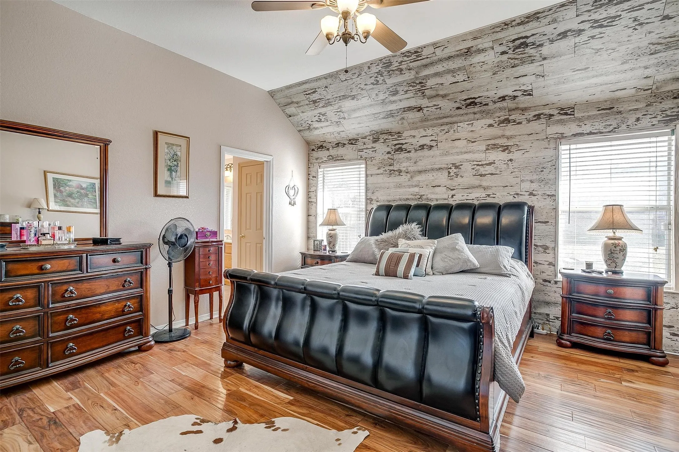 Bedroom featuring light wood finished floors, vaulted ceiling, an accent wall, ceiling fan, and wooden walls