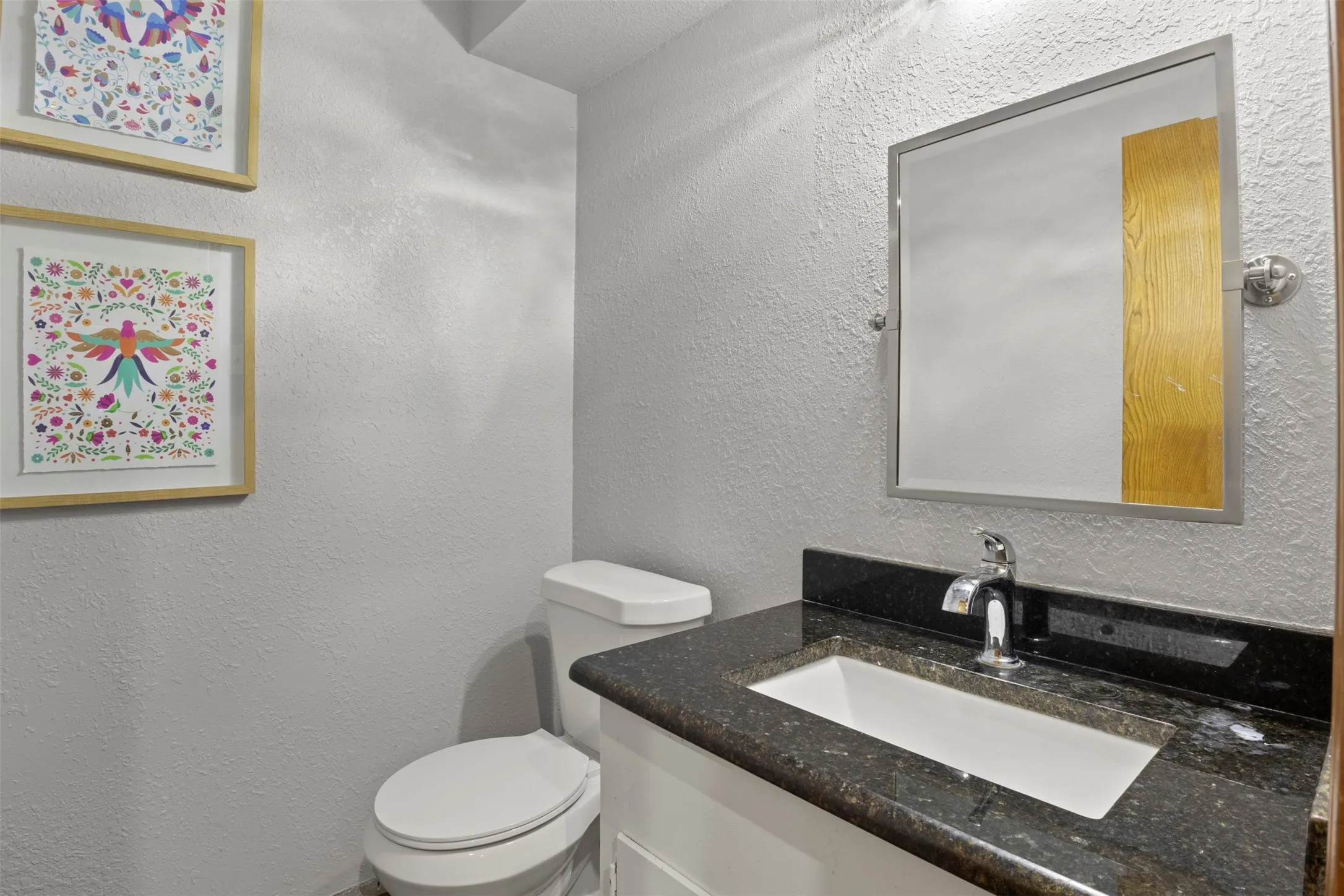 Bathroom featuring a white vanity with an undermount sink, dark speckled countertop, and chrome faucet