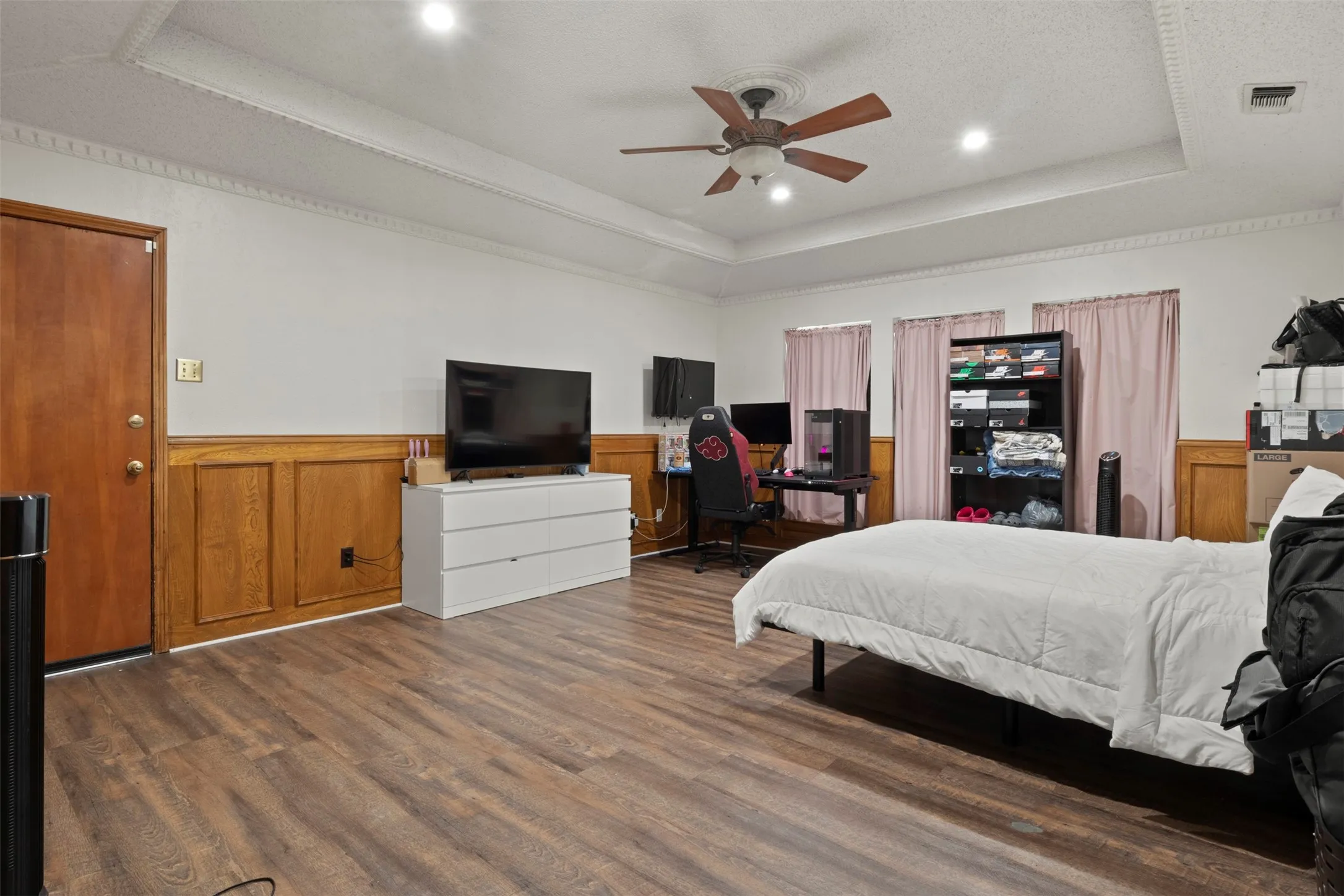 Spacious room featuring wood-finish flooring, half-wall wood paneling, and a tray ceiling with recessed lighting