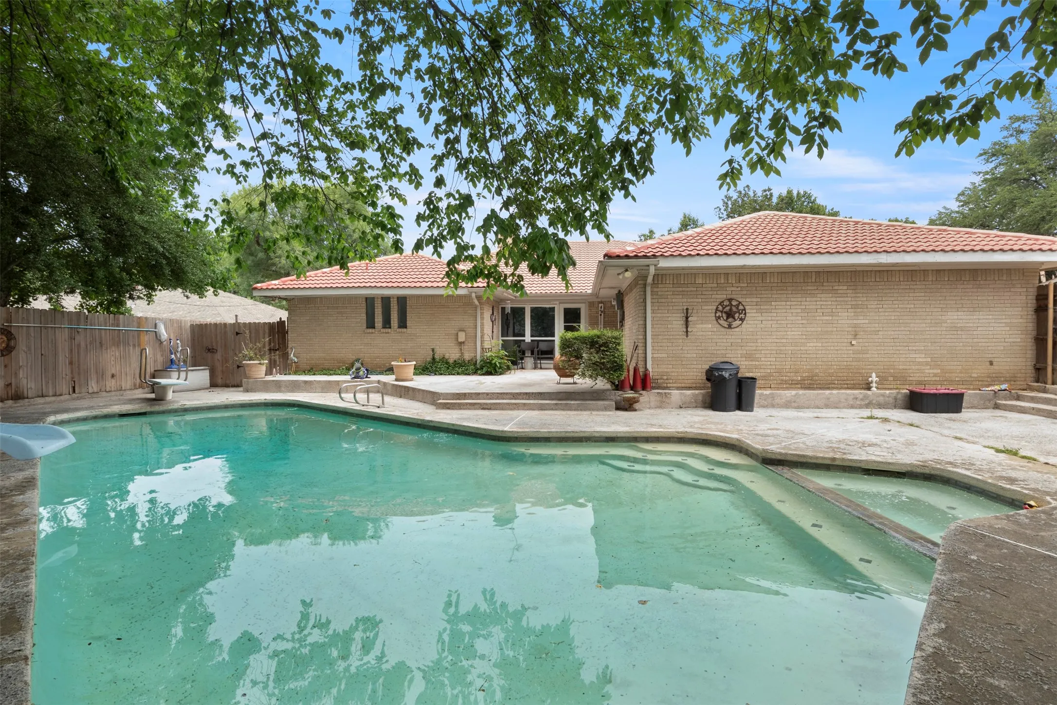 Expansive outdoor swimming pool with concrete decking, surrounded by a light-colored brick exterior and a red tile roof