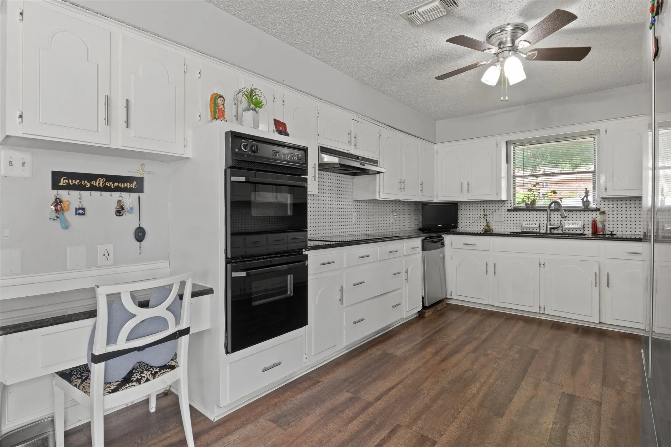 Bright kitchen featuring white cabinetry, dark countertops, wood-finish flooring, a built-in double oven, and a ceiling fan with integrated lighting