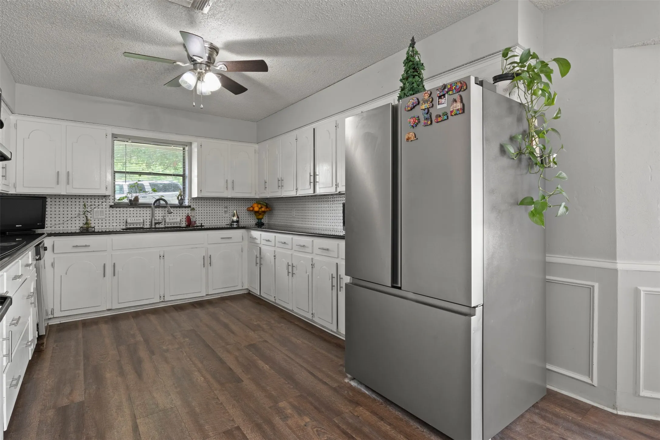 Kitchen featuring wood-finish flooring, white cabinetry, black countertops, and a white tiled backsplash