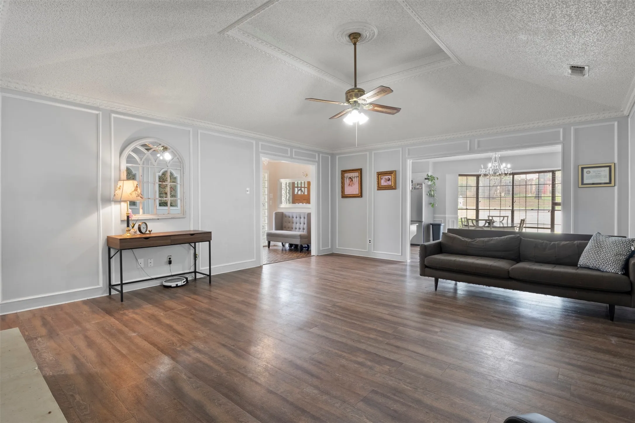 Spacious living area featuring wood-finish flooring, vaulted ceilings, decorative crown molding, and wainscoting