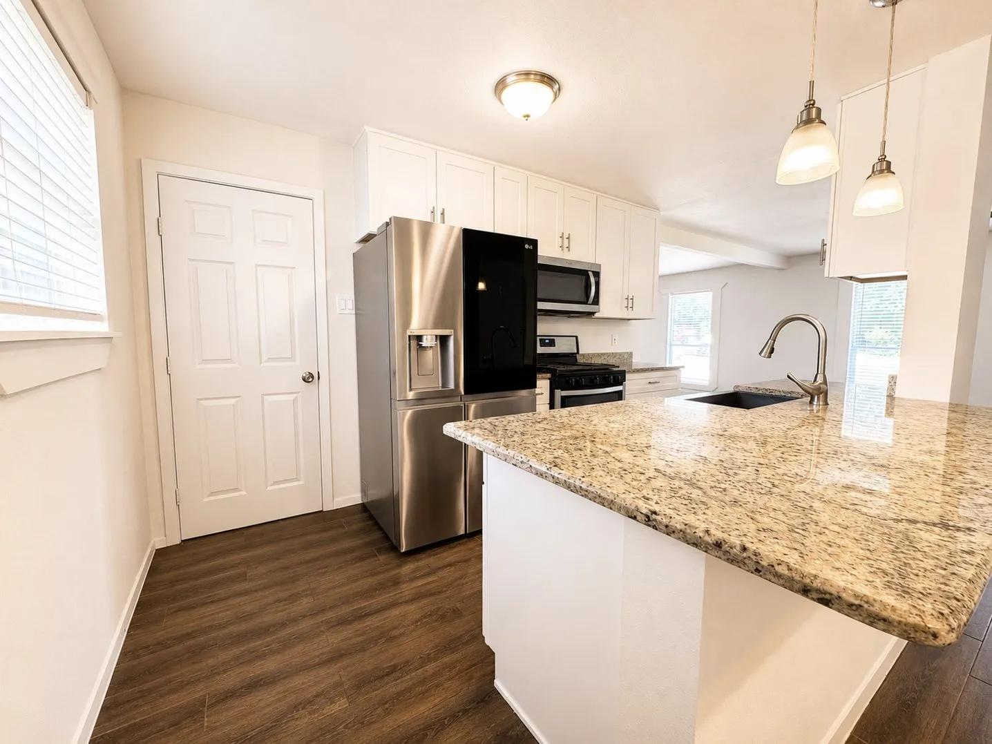 Kitchen featuring an island with stone countertop, stainless steel appliances, white cabinetry, wood-finish flooring, and recessed lighting