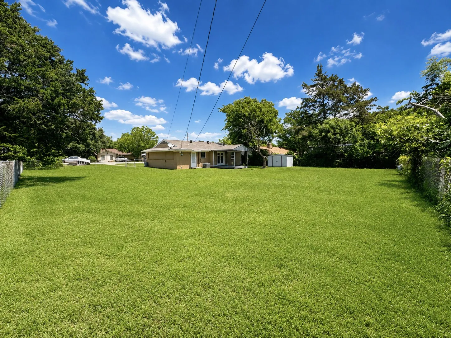 Expansive, level backyard featuring a manicured lawn, partial chain-link fencing, and mature perimeter trees
