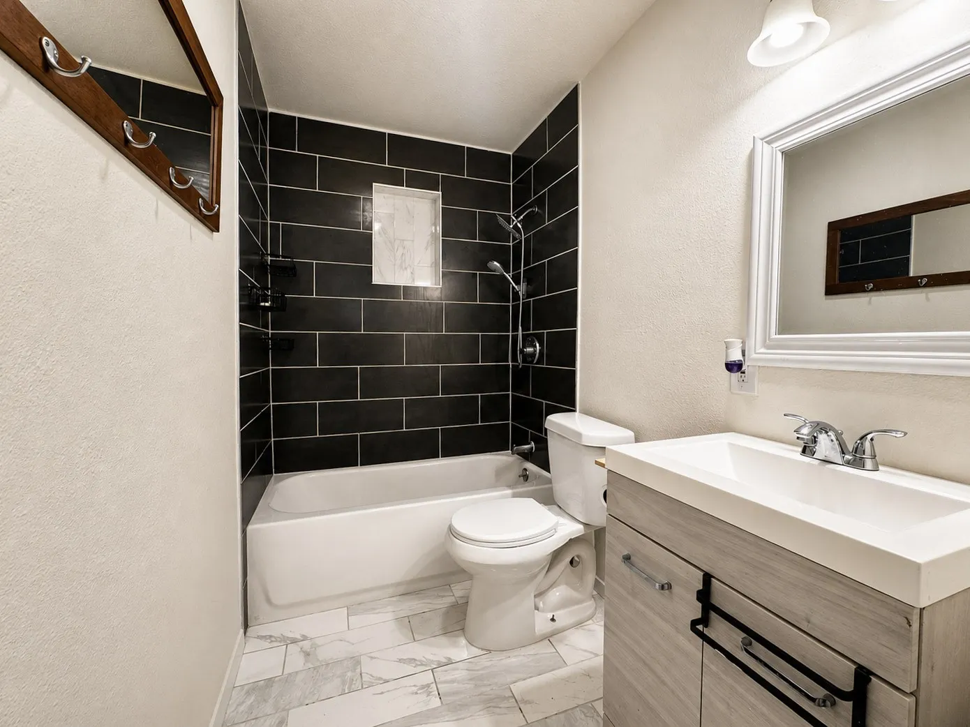 Bathroom featuring a bathtub with black subway tile surround, a built-in shower niche, and a chrome shower head with handheld sprayer