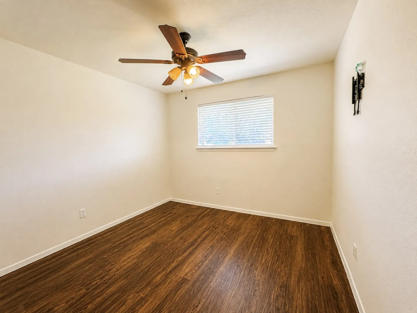 Room featuring wood-finish flooring, a ceiling fan with integrated lighting, and a window with horizontal blinds