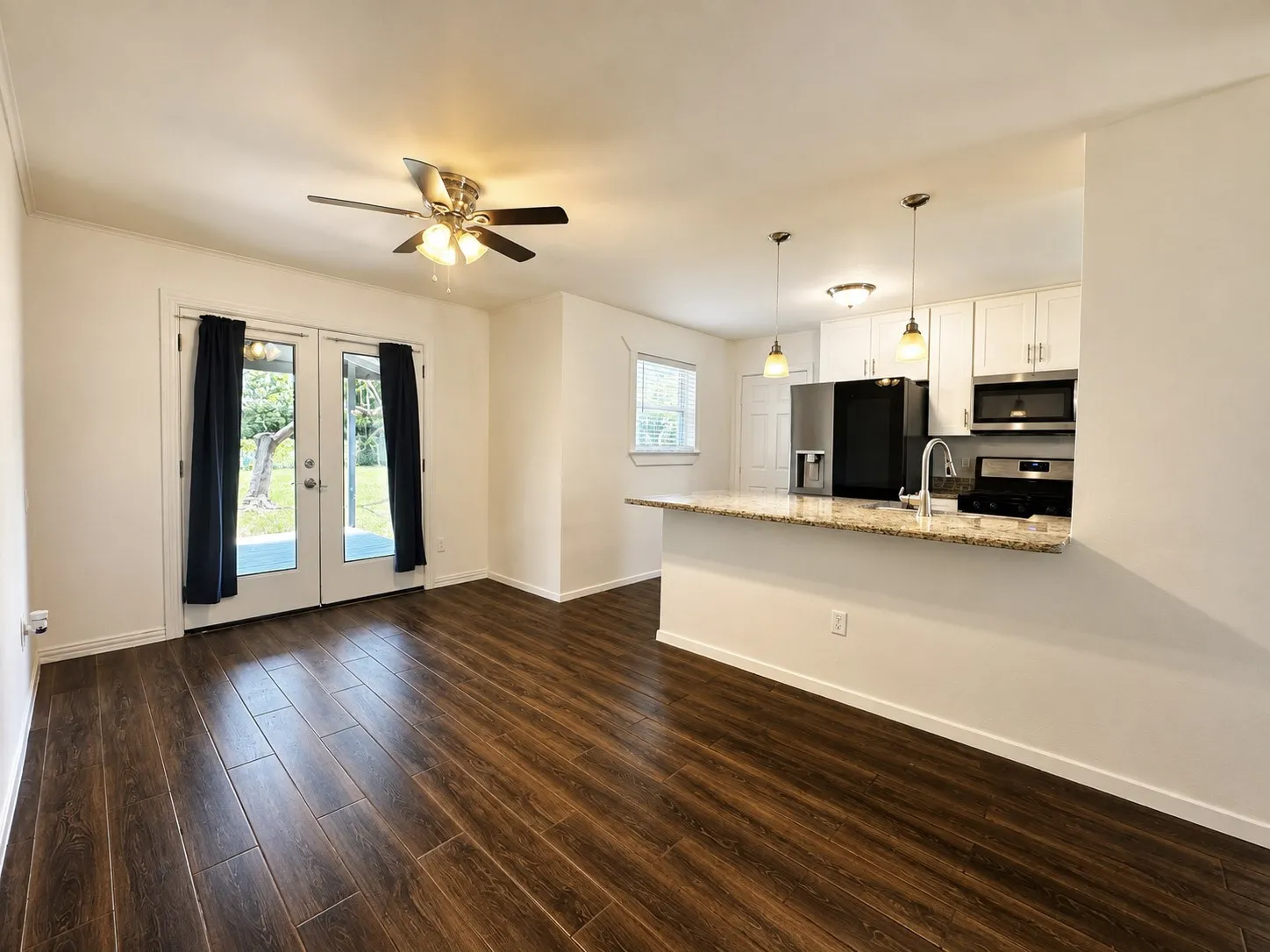 Open concept living area featuring wood-finish flooring, a ceiling fan with integrated lighting, and French doors providing access to the exterior