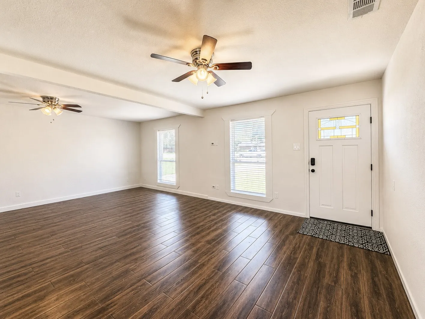 Spacious room featuring wood-finish flooring, white walls, and a white entry door with frosted glass detailing