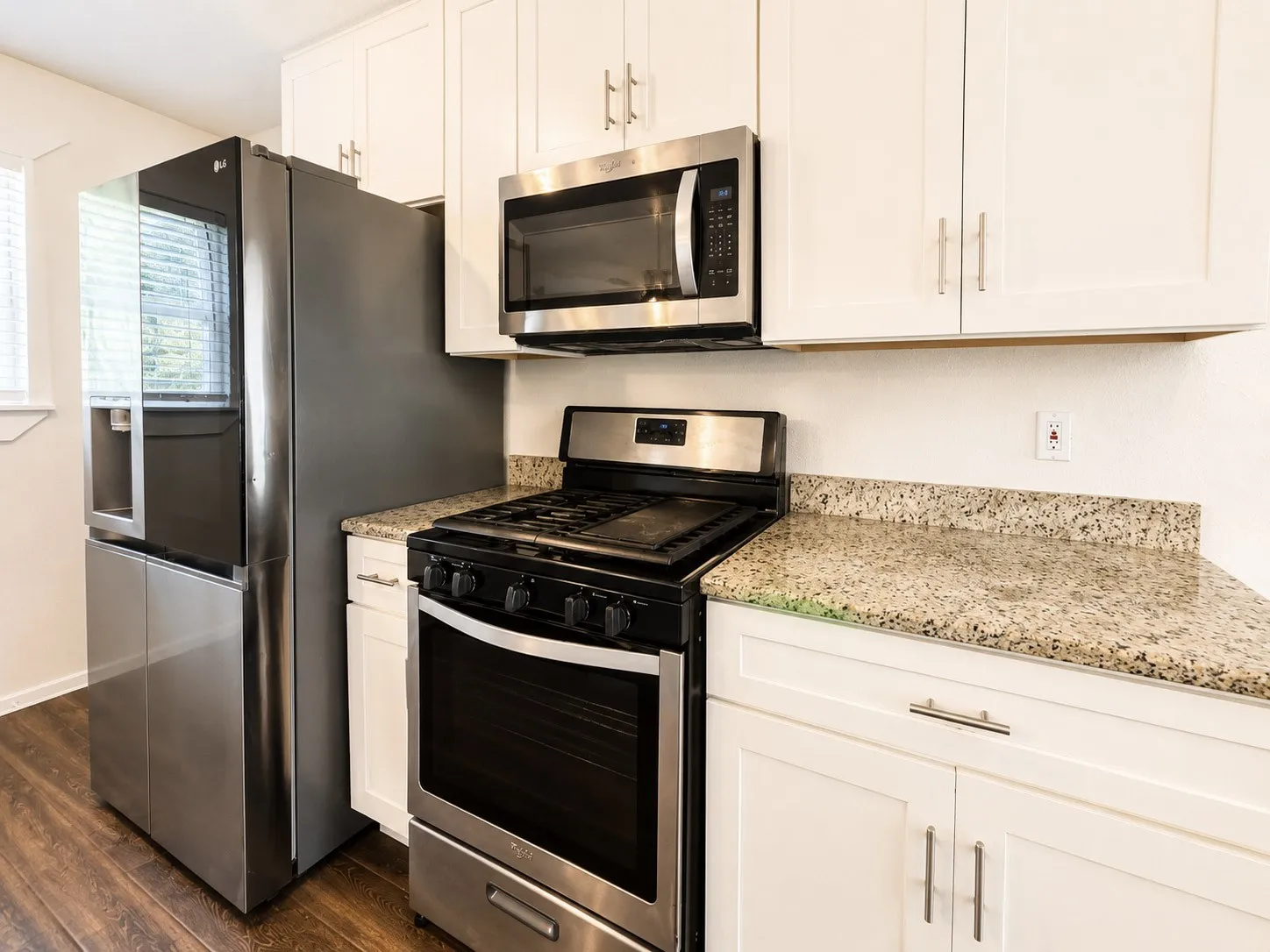 Kitchen featuring stainless steel appliances, white cabinetry, granite countertops, and wood-finish flooring