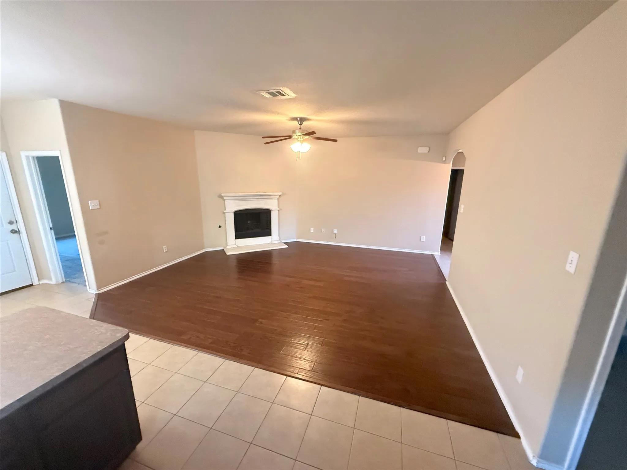 Spacious interior with wood-finish flooring, a traditional fireplace with a white mantel, and a ceiling fan with integrated lighting