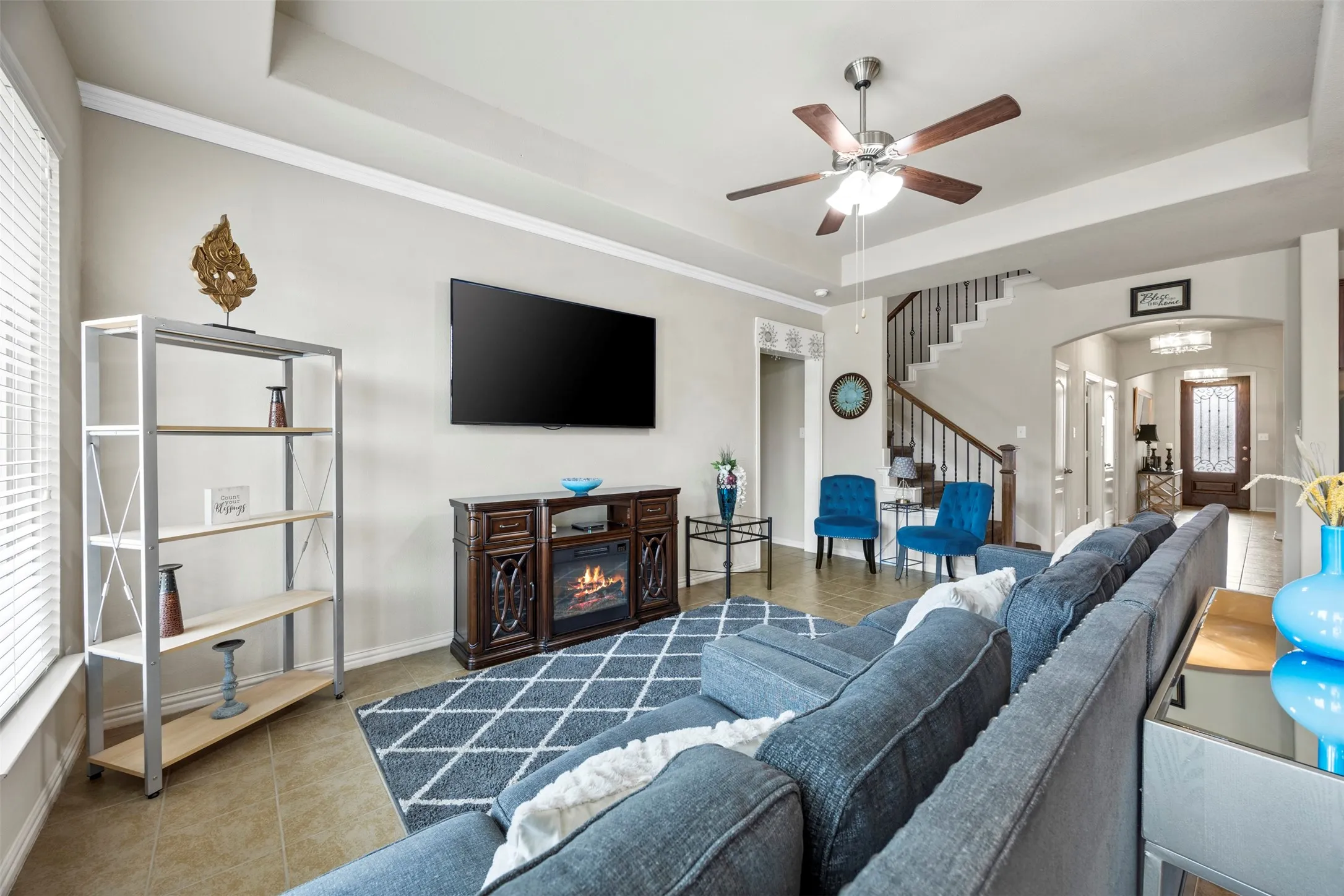 Open concept living space featuring tile flooring, crown molding, a ceiling fan with integrated lighting, and an elegant staircase with wood and wrought iron balusters