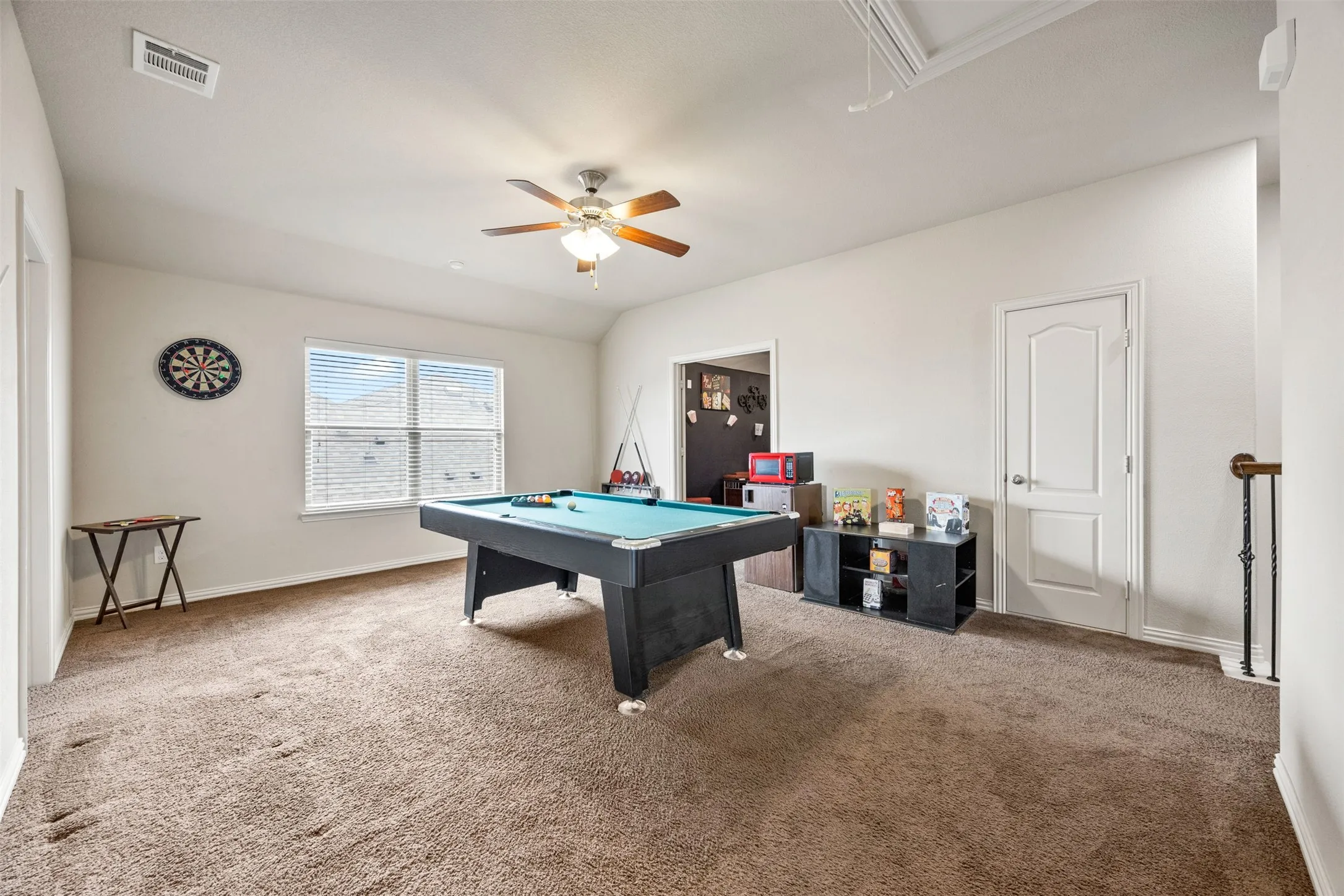 Spacious room featuring neutral carpeting, a large window with horizontal blinds, and a ceiling fan with integrated lighting
