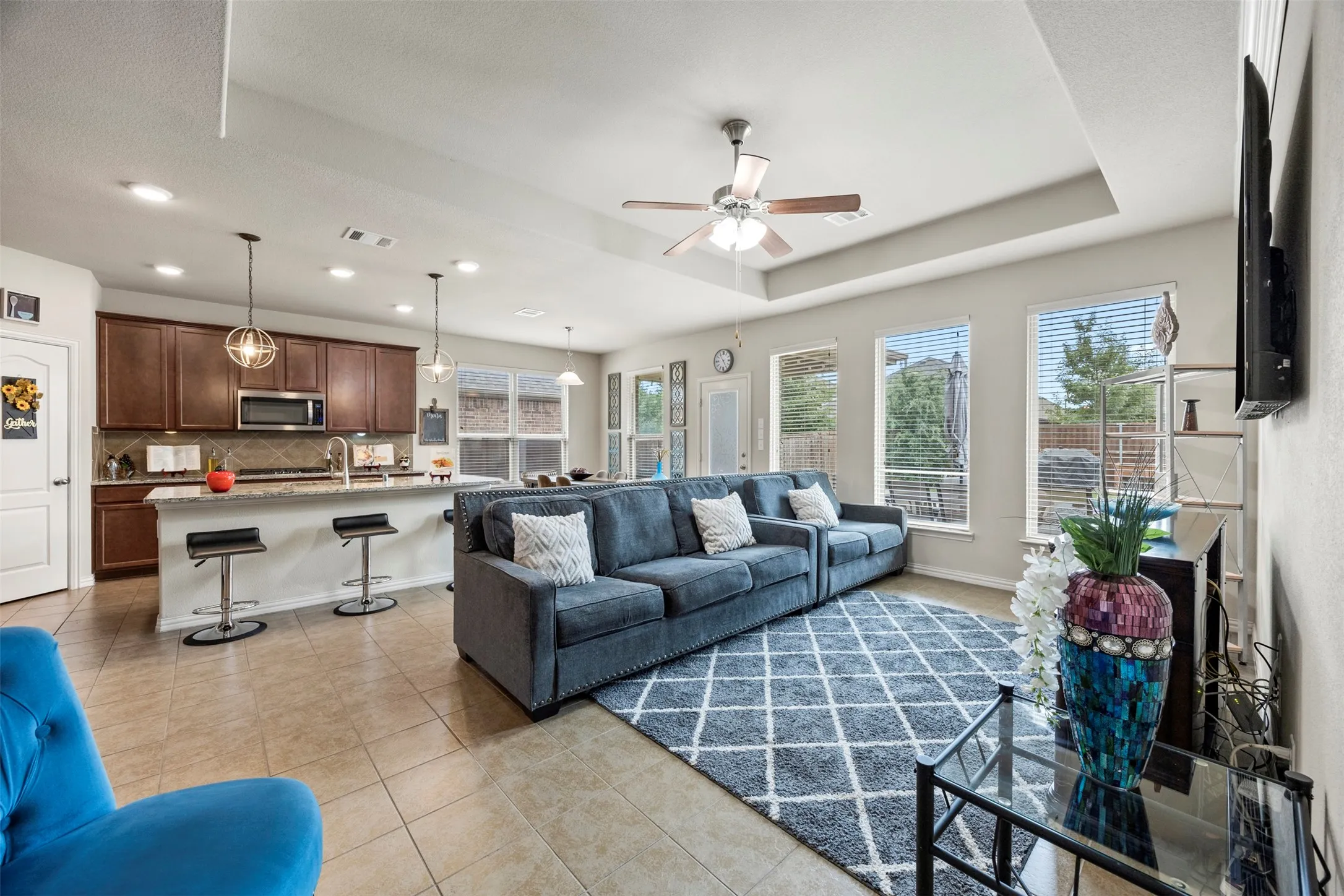 Open-concept living area featuring tile flooring, a tray ceiling, and multiple windows
