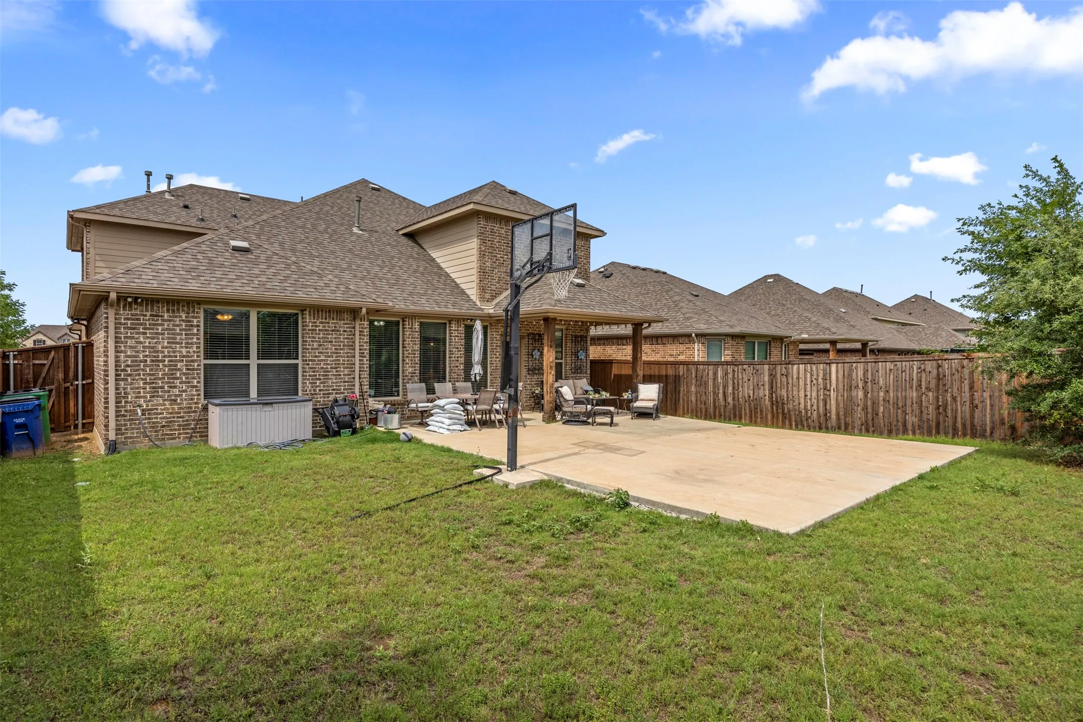Expansive backyard featuring a large concrete patio, a wood privacy fence, and a two-story brick exterior with siding accents