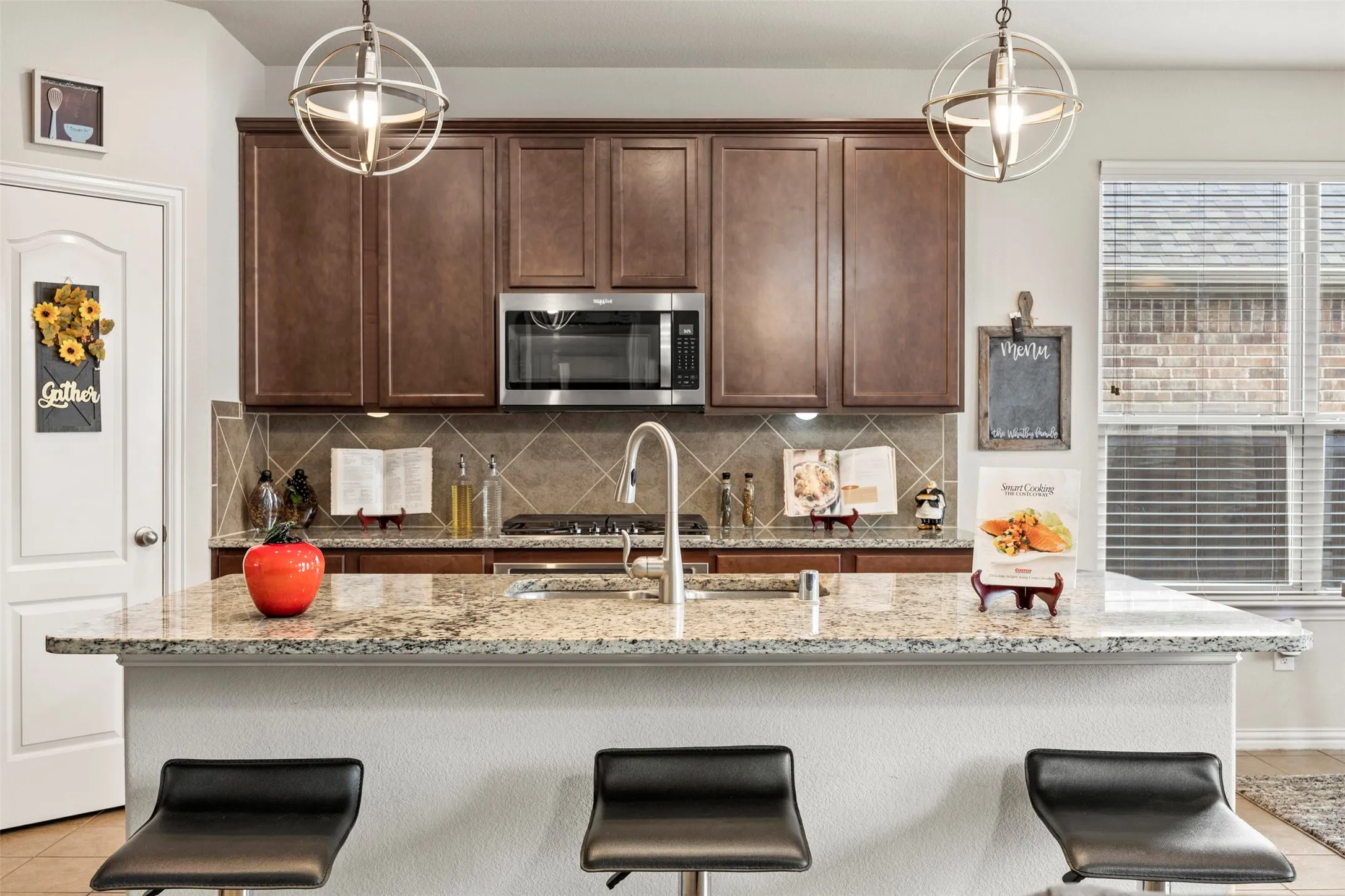 Kitchen featuring a granite-topped island with seating, dark wood cabinetry, stainless steel appliances, and a tile backsplash