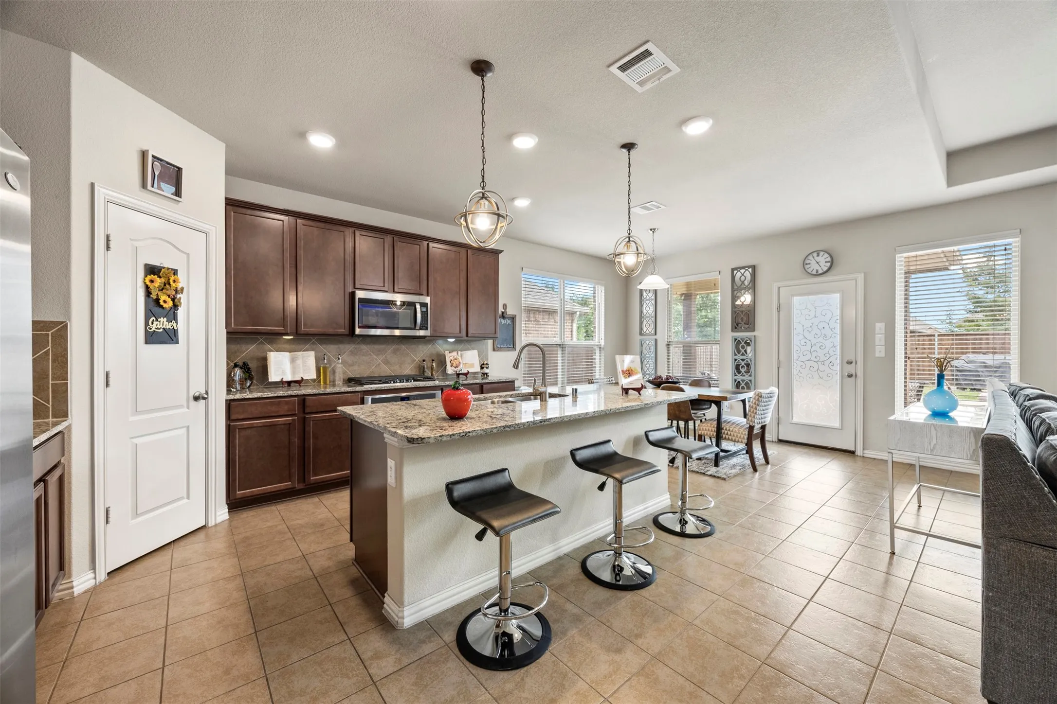 Kitchen featuring dark wood cabinetry, a granite-topped island with seating, stainless steel appliances, and tile flooring