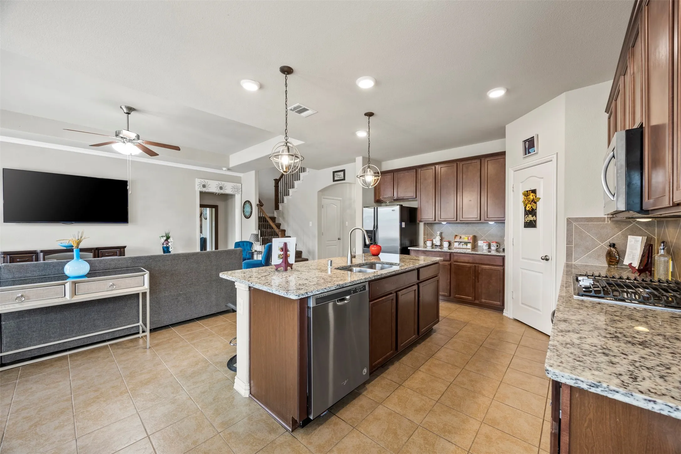 Kitchen island featuring granite countertops, a stainless steel double sink, and pendant lighting