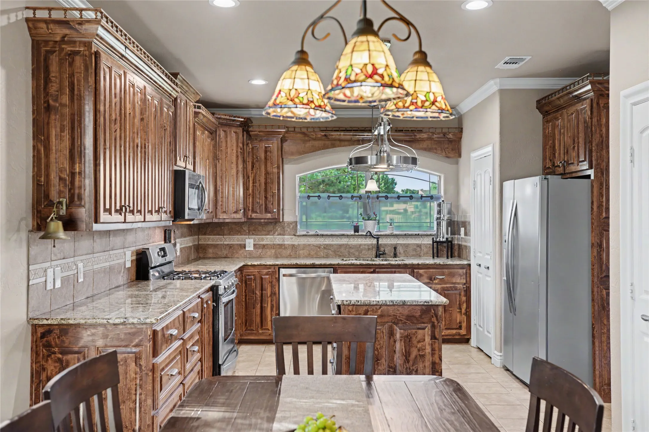 Kitchen featuring extensive wood cabinetry with crown molding, granite countertops, an undermount sink, stainless steel appliances, and tile flooring
