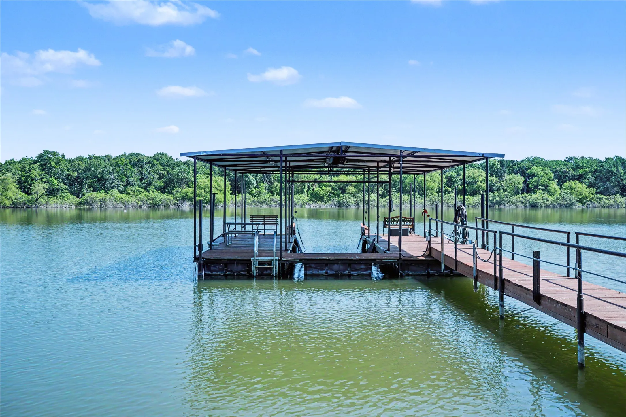 Covered boat dock featuring a metal frame, wood-finish decking, and a gangway with black metal railing