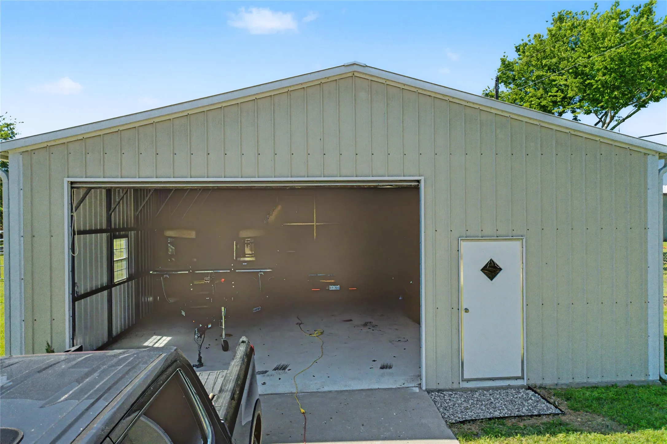 Metal-sided outbuilding with a prominent overhead door opening, an additional pedestrian entry door, and a single window
