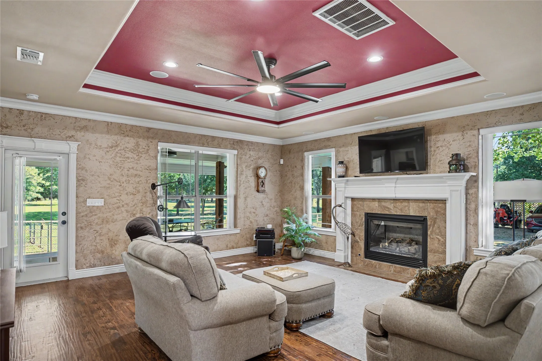 Living area featuring wood-finish flooring, a tray ceiling with recessed lighting and a ceiling fan, and multiple windows
