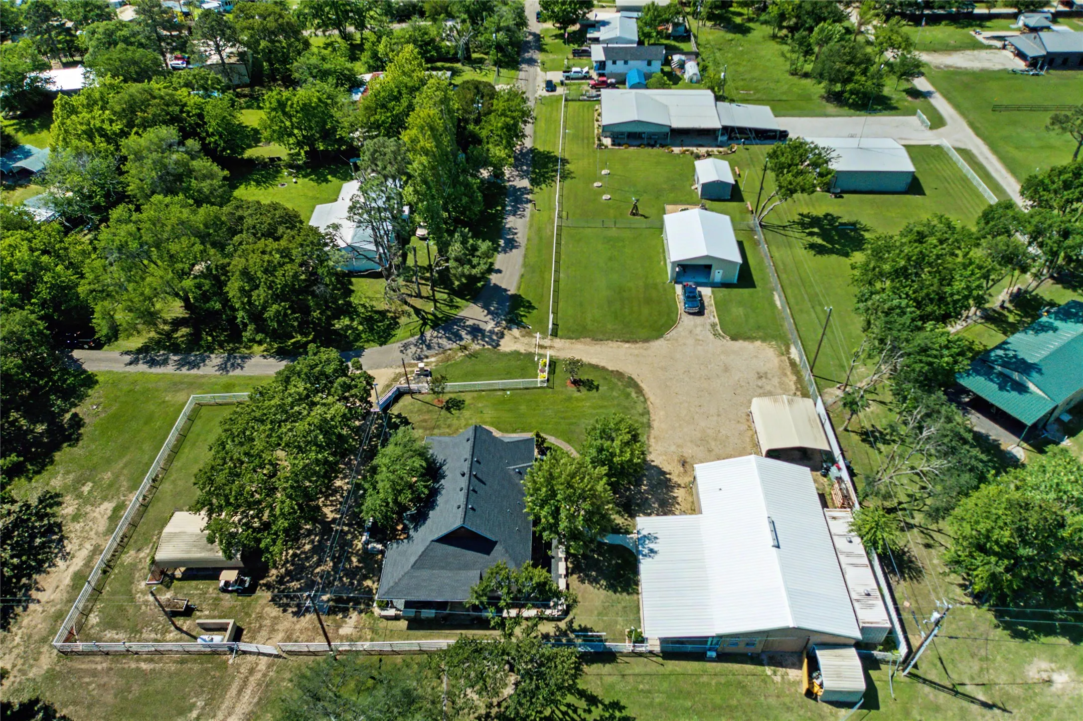 Expansive property featuring a main residence with a dark shingle roof, accompanied by multiple outbuildings including a large metal structure with a silver roof, and a smaller metal building