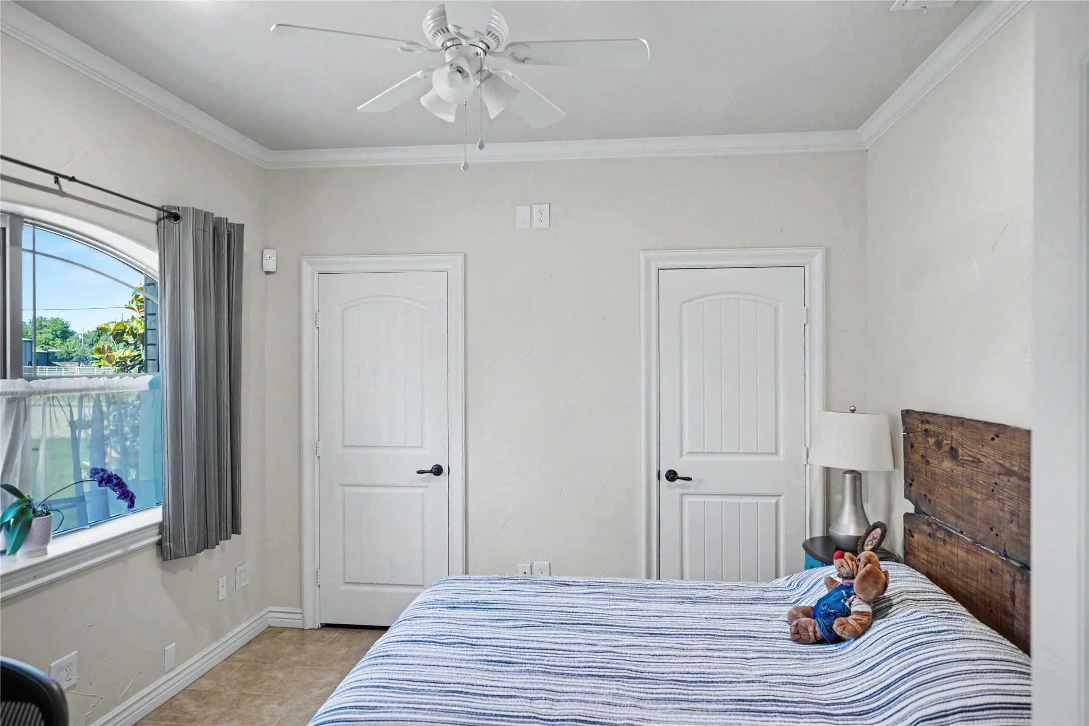 Neutral-toned room featuring crown molding, an arched window, and two paneled doors with dark hardware