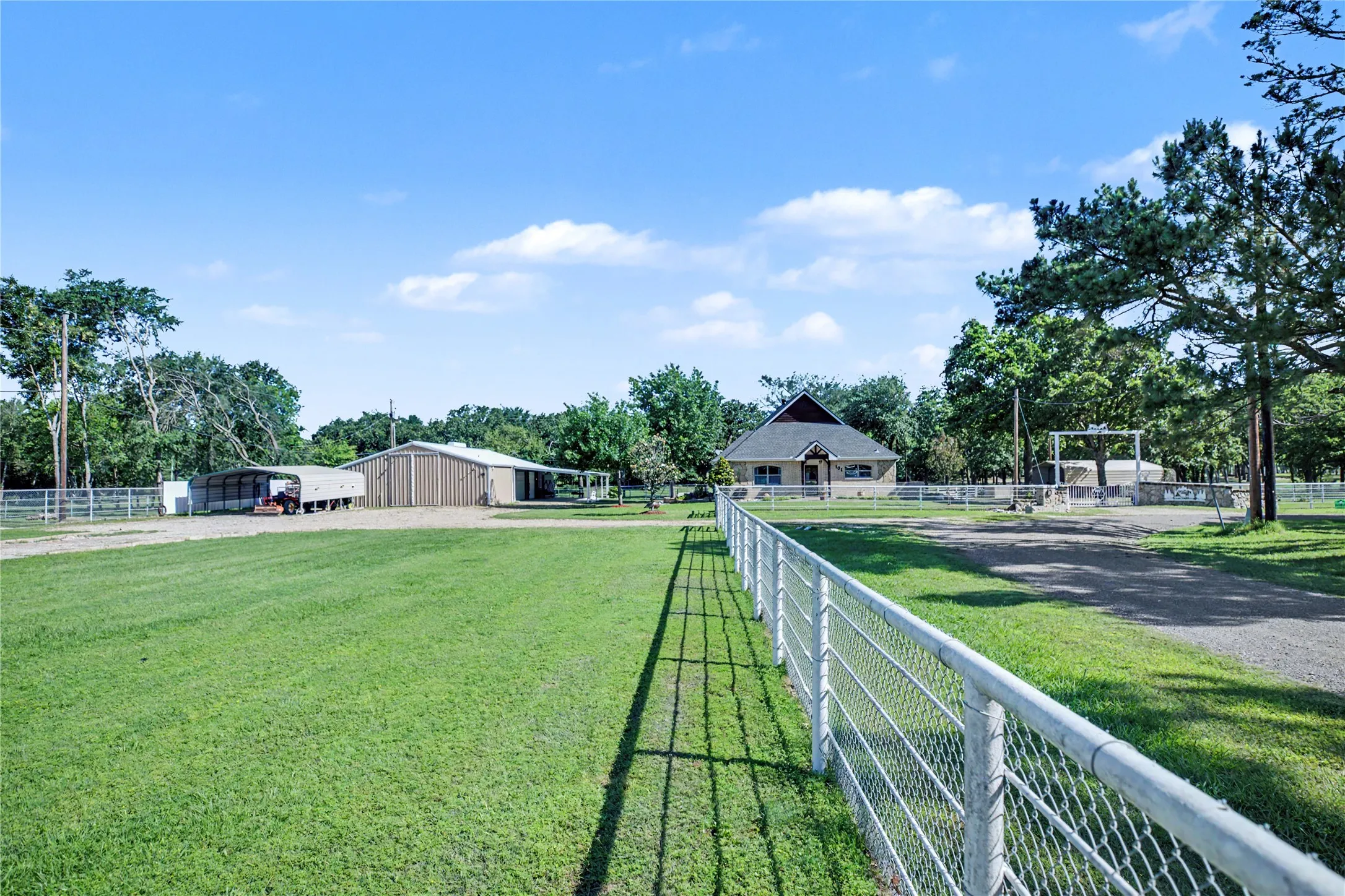 Expansive green grounds featuring a white metal fence, multiple outbuildings, and a main residence with a prominent roofline