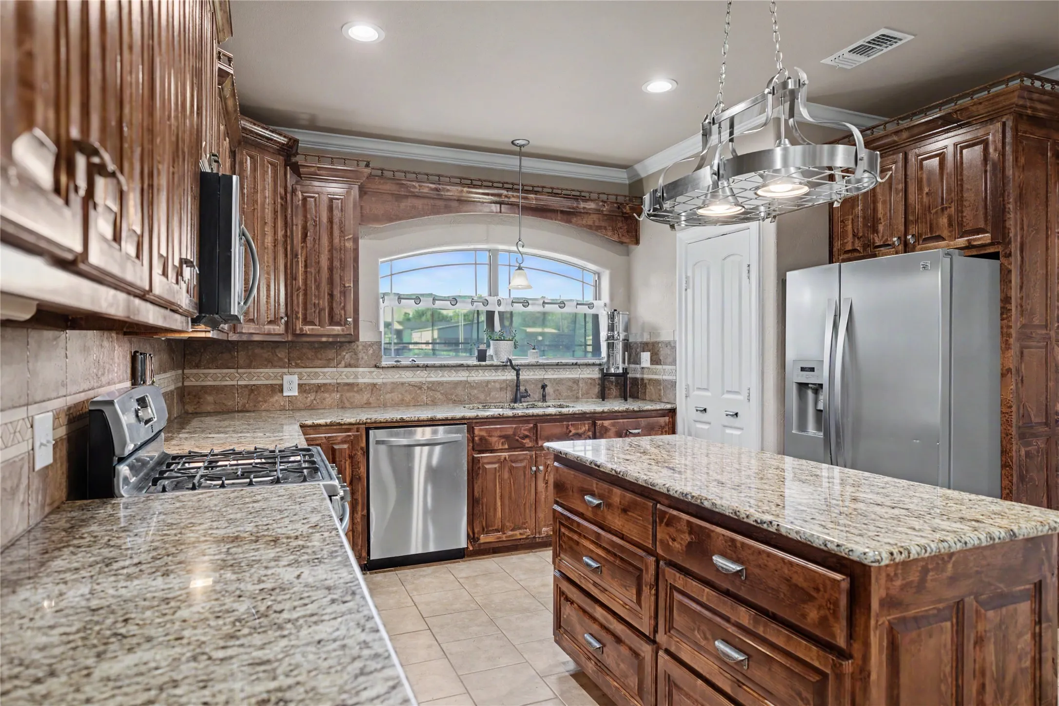 Kitchen featuring a central island with storage, granite countertops, stainless steel appliances, rich wood cabinetry, and a pot rack light fixture