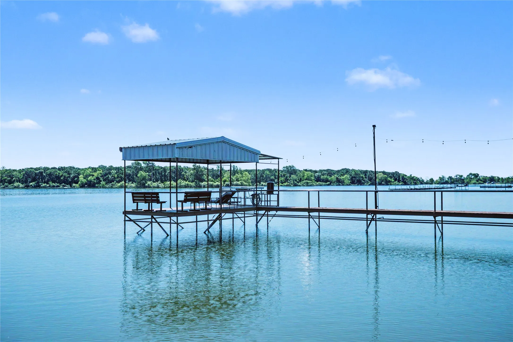 Private dock featuring a covered seating area with a metal roof, open-air walkway, and string lighting