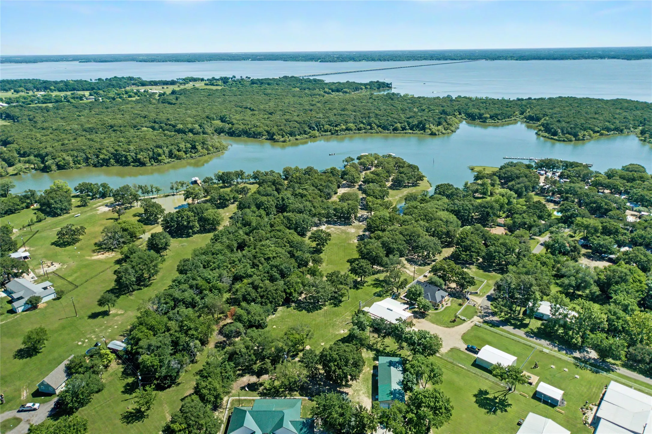 Expansive aerial showcasing a body of water, lush green trees, and scattered residential properties