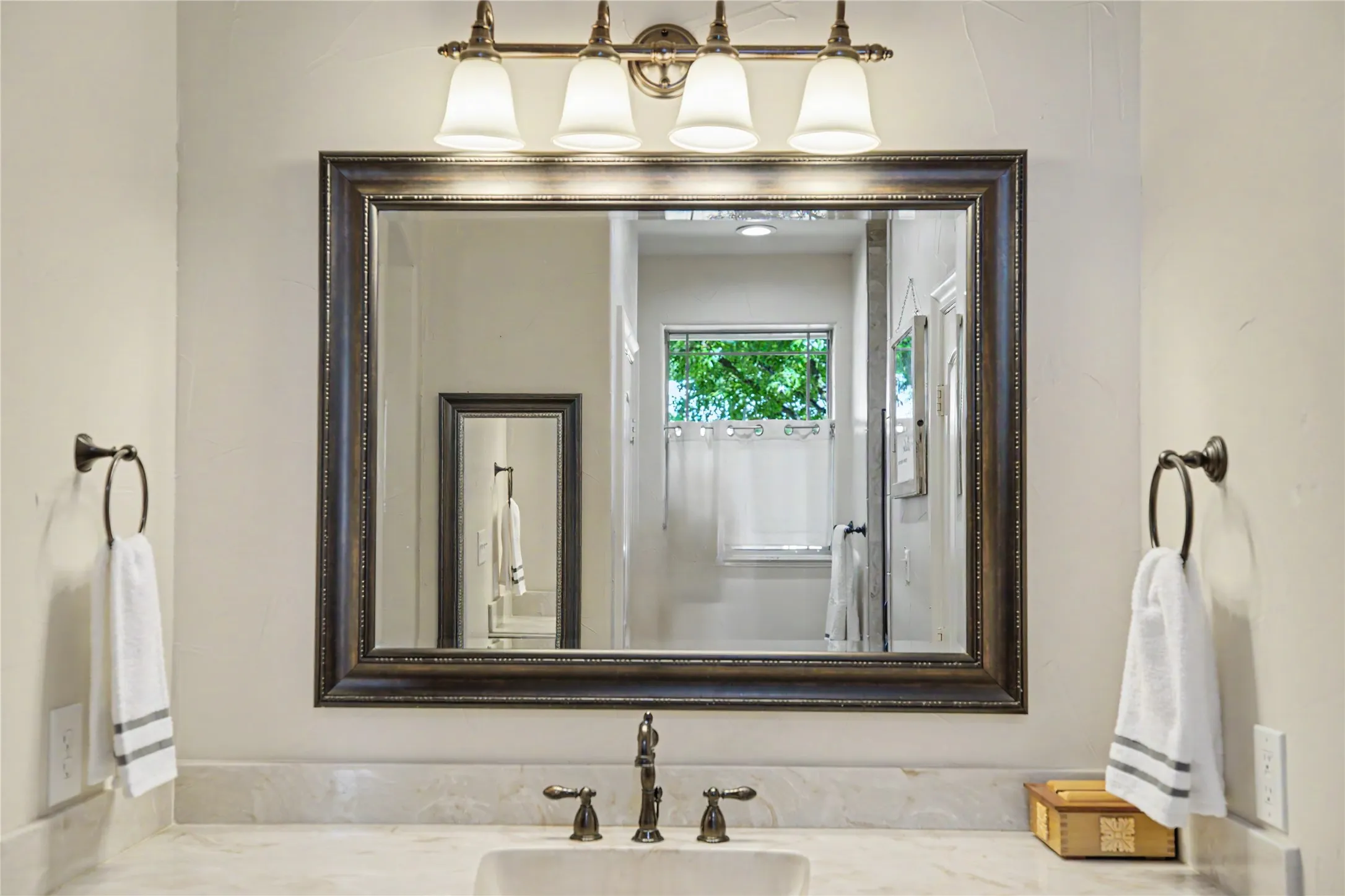 Bathroom vanity featuring a framed mirror, four-light fixture with frosted glass shades, and a bronze-finish faucet