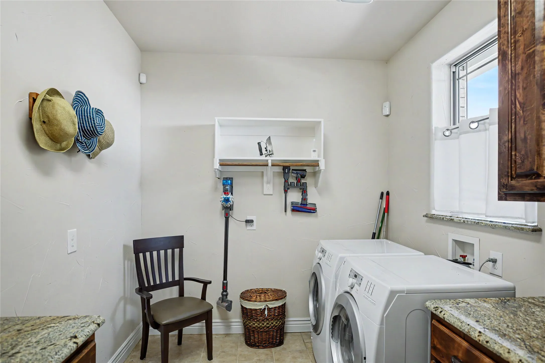 Laundry area featuring light-toned walls, a window with a stone-finish sill, and built-in white shelving