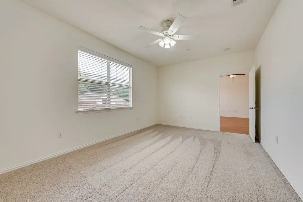 Carpeted room featuring a ceiling fan with integrated lighting, a window with horizontal blinds, and a doorway opening to a room with wood-finish flooring