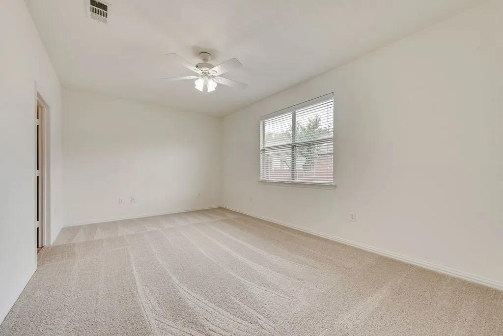 Carpeted room featuring a ceiling fan with light fixture, neutral wall colors, and a window with blinds