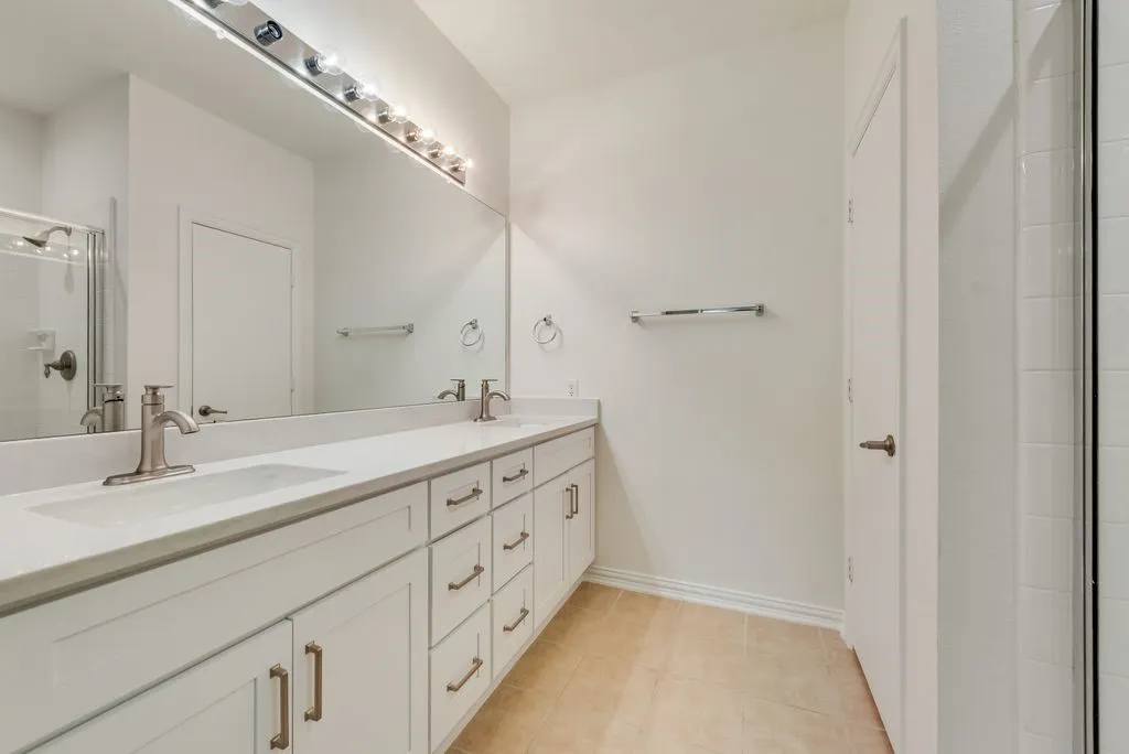 Double vanity featuring white cabinetry with brushed nickel hardware, light-toned countertops, and dual undermount sinks with brushed nickel faucets