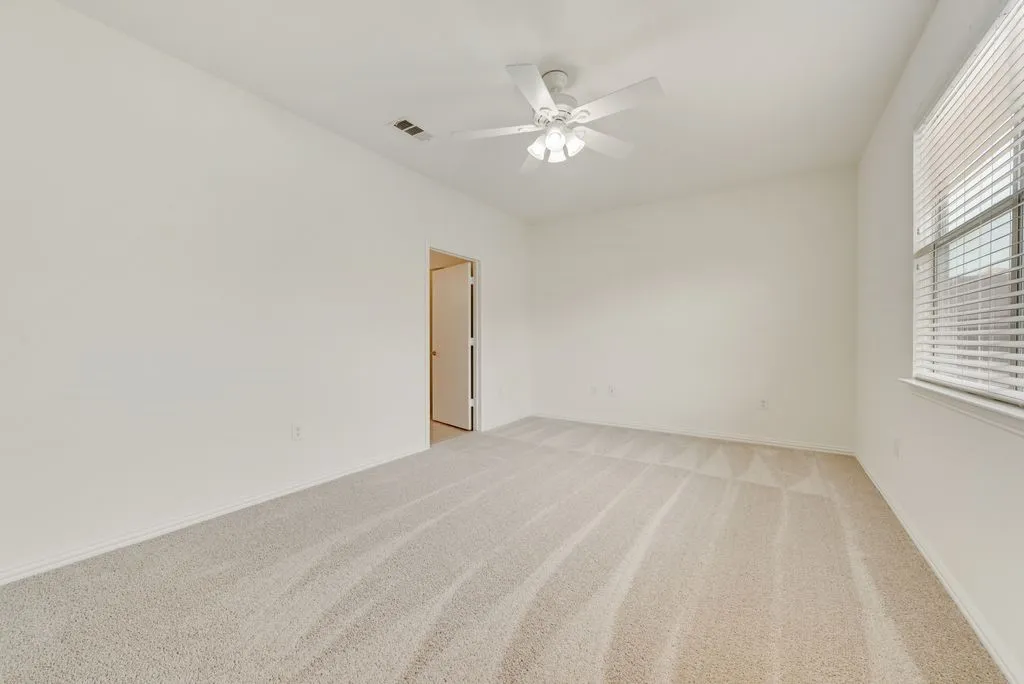 Spacious interior room featuring light-toned carpeting, white walls, and a ceiling fan with integrated lighting