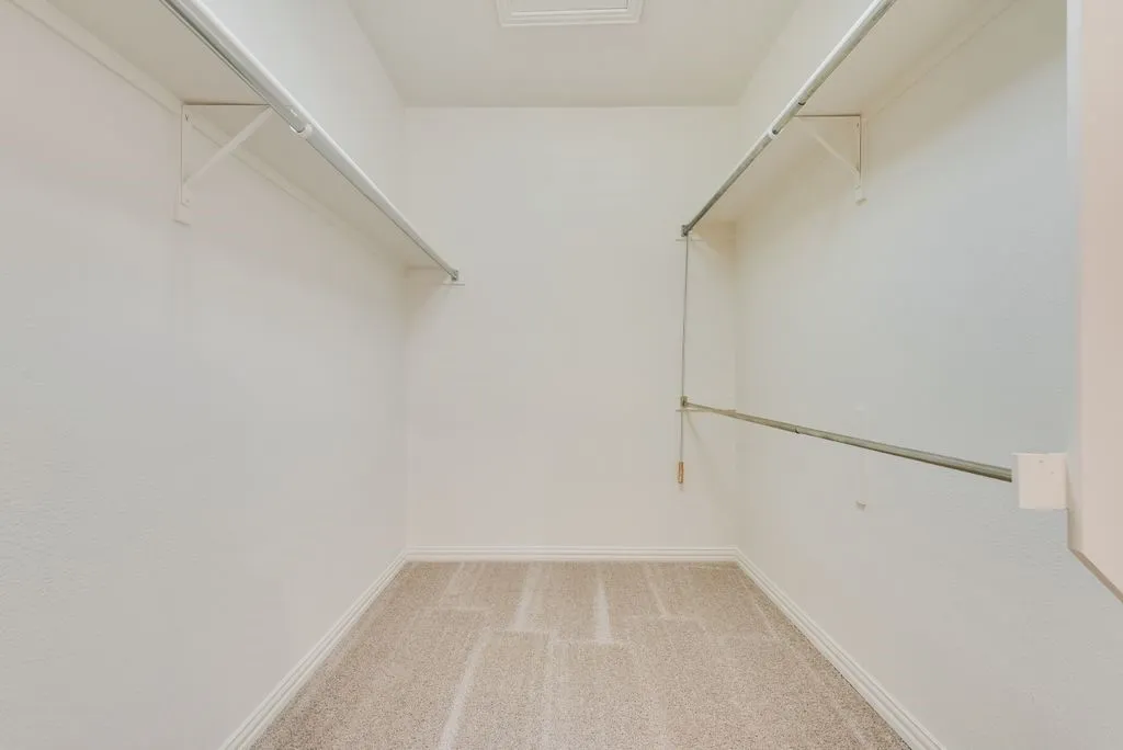 Walk-in closet featuring light-toned carpet flooring, white baseboards, textured white walls, and built-in shelving with hanging rods