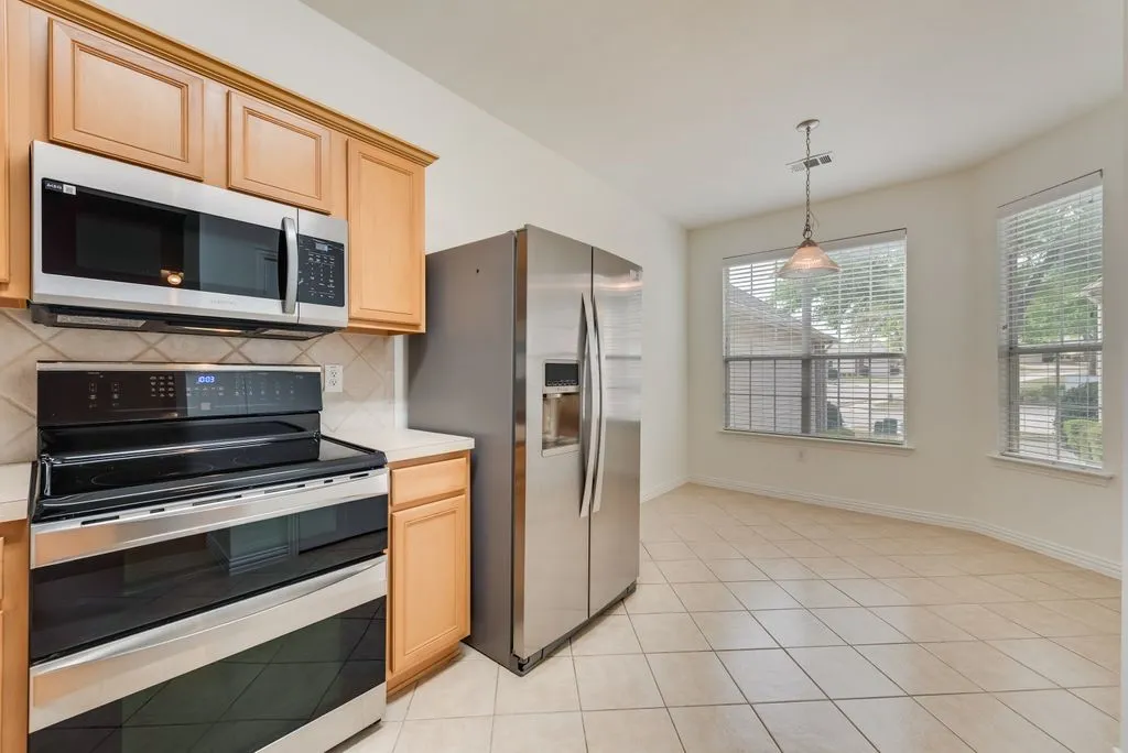 Kitchen area featuring light wood cabinetry, stainless steel appliances, and a tiled backsplash