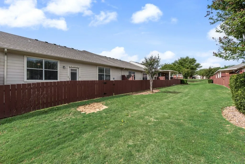 Expansive lawn area featuring a brown privacy fence, mature trees, and a paved walkway
