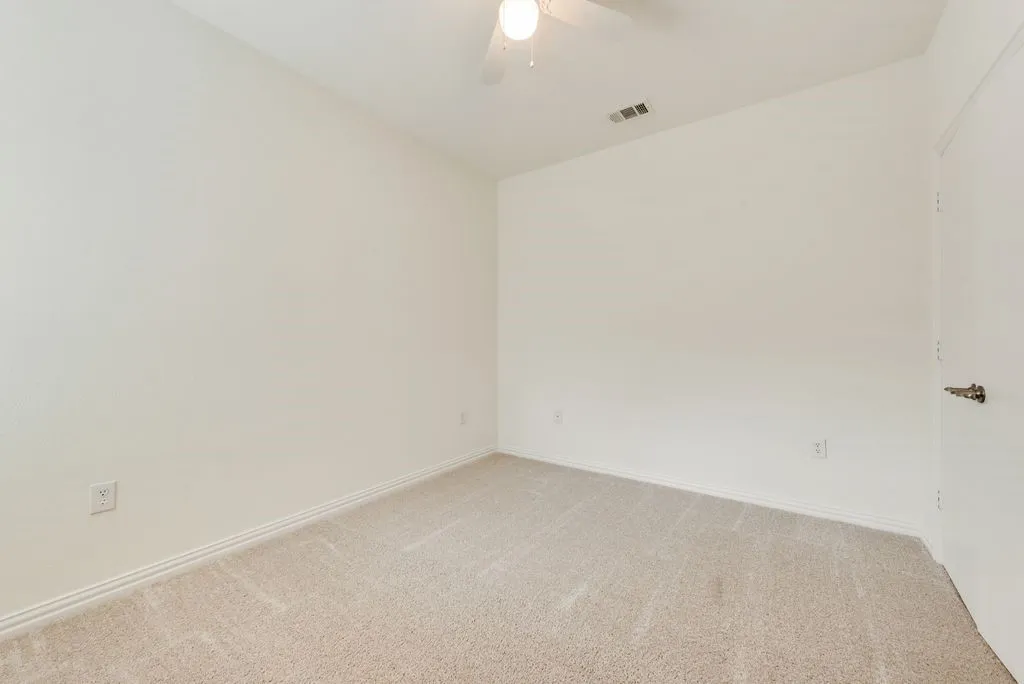 Carpeted room featuring white walls, white baseboards, a ceiling fan, and a white door with a brass-finish handle