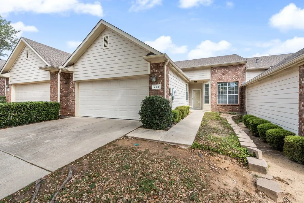 Exterior featuring brick and siding finishes, an attached garage, a concrete driveway, a front entry walkway, and established shrubbery