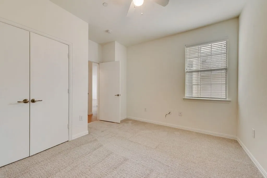 Carpeted interior space featuring a window with blinds, ceiling fan, and white walls