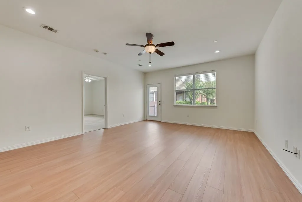 Spacious room featuring wood-finish flooring, a ceiling fan, recessed lighting, and a large window with blinds